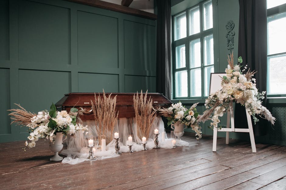 An elegant floral arrangement featuring white and cream blossoms, including roses and lilies, complemented by soft beige pampas grass and greenery, arranged in white vases. The bouquet is placed on th